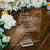 Acrylic audio guestbook sign displayed on outdoor wedding reception welcome table with guest instructions